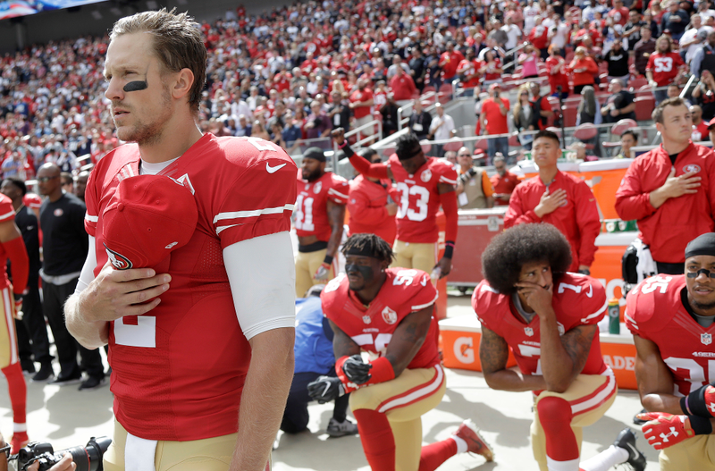 In this Oct. 2, 2016, file photo, San Francisco 49ers quarterback Blaine Gabbert, left, stands as outside linebacker Eli Harold, from bottom left, quarterback Colin Kaepernick and safety Eric Reid kneel during the national anthem before an NFL football game against the Dallas Cowboys in Santa Clara, Calif.